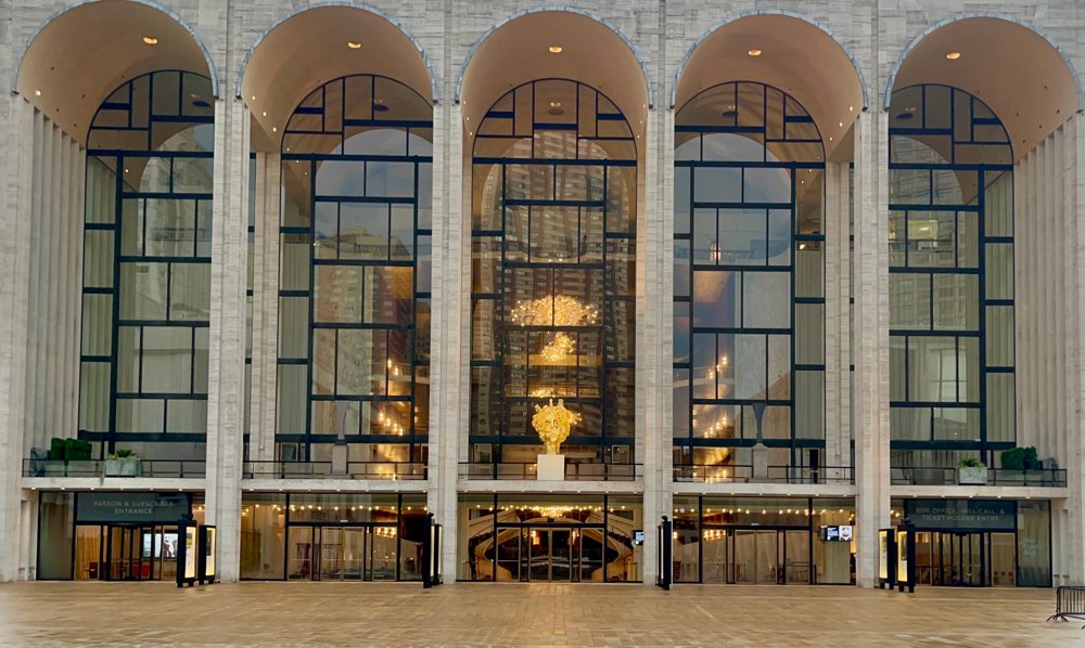 The arched glass facade of an opera house in New York, lit gold at dusk